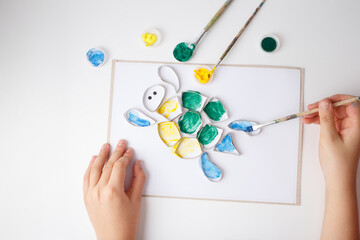 a creative art activity where a hand is painting a turtle-shaped stencil on a piece of paper.