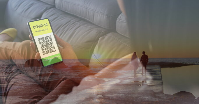 Image of woman with covid passport on smartphone over couple on beach