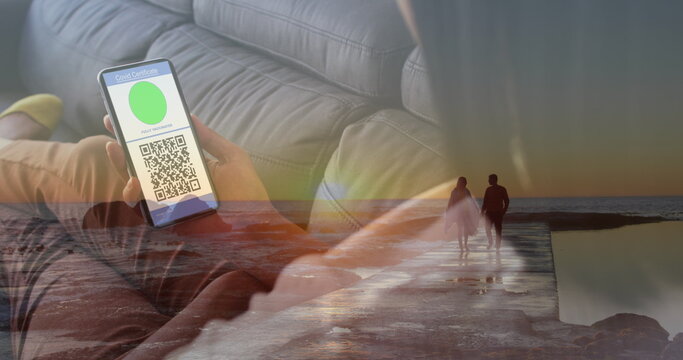 Image of woman with covid passport on smartphone over couple on beach