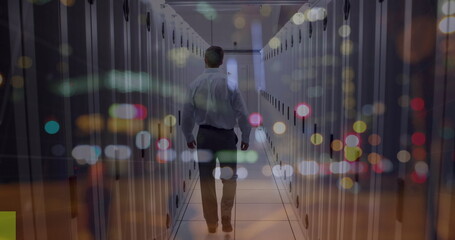 Walking IT technician wearing shirt navigating data center aisle with LED lights on server racks