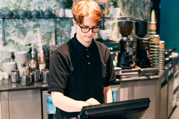 Young waiter serving customer at cash point in cafe. Man working with POS terminal. Cashier,...