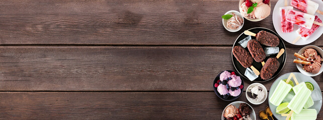 Cool summer food side border. Assortment of ice cream bowls, popsicles and frozen treats. Overhead view on a dark wood banner background. Copy space.