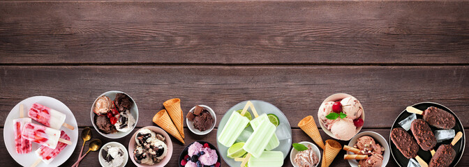 Cool summer food bottom border. Variety of ice cream bowls, popsicles and frozen treats. Top view on a dark wood banner background. Copy space.
