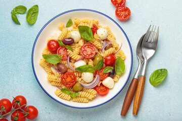 Plate with Italian fusilli pasta salad with fresh cherry tomatoes, mozzarella, olives, red onion, and basil leaves, concept of Italian culinary tradition