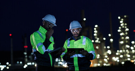 Industrial System Engineers Discussing Over Laptop And Digital Tablet While work over night at Refinery and gas petrochemical plant