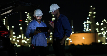 Two college Industrial engineer with white safety hat work with digital tablet and walkie talkie on night shift at Refinery and gas petrochemical plant, Industrial and business
