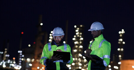 Industrial System Engineers Discussing Over Laptop And Digital Tablet While work over night at Refinery and gas petrochemical plant