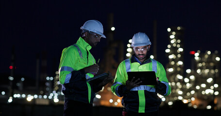 Industrial System Engineers Discussing Over Laptop And Digital Tablet While work over night at Refinery and gas petrochemical plant