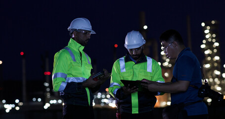 Industrial System Engineers Discussing Over Laptop And Digital Tablet While work over night at Refinery and gas petrochemical plant