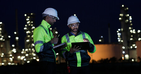 Industrial System Engineers Discussing Over Laptop And Digital Tablet While work over night at Refinery and gas petrochemical plant