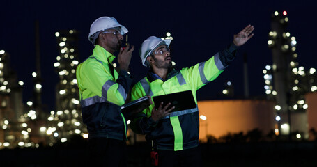 Industrial System Engineers Discussing Over Laptop And Digital Tablet While work over night at Refinery and gas petrochemical plant