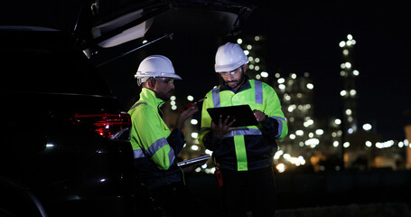 Industrial System Engineers Discussing Over Laptop And Digital Tablet While work over night at Refinery and gas petrochemical plant