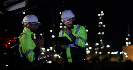 Industrial System Engineers Discussing Over Laptop And Digital Tablet While work over night at Refinery and gas petrochemical plant