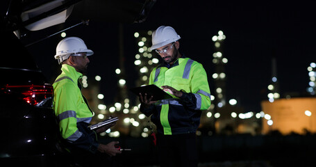 Industrial System Engineers Discussing Over Laptop And Digital Tablet While work over night at Refinery and gas petrochemical plant