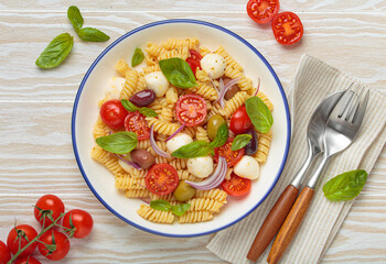 Plate with Italian fusilli pasta salad with fresh cherry tomatoes, mozzarella, olives, red onion, and basil leaves, concept of Italian culinary tradition