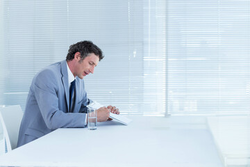 Middle-aged man in suit signing document at conference table with pen and water glass, copy space