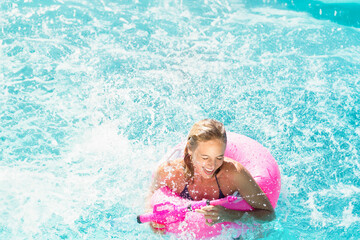 Pink inflatable ring floating in turquoise pool with water splashing and foaming in sunlight