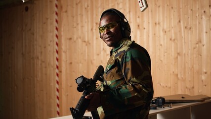 Portrait of happy soldier holding assault rifle, developing marksmanship skills in firing range....