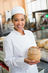 Baked round loaf resting on stainless steel table in bright bakery kitchen with ovens racks mixers