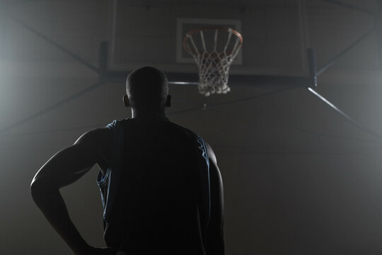 Fototapeta Basketball player standing at free-throw line in gym, looking up at hoop mounted on metal beams