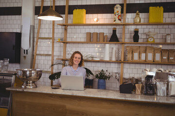 Woman in blue shirt working on laptop in coffee shop at marble counter beside yellow bins