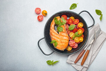 Grilled salmon steak on a black pan, accompanied by vibrant cherry tomatoes and fresh basil leaves, healthy eating or diet concept, copy space