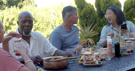 Senior diverse friends enjoying in garden lunch, talking and sharing stories at garden table