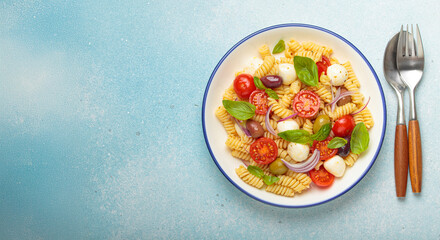 Plate with Italian fusilli pasta salad with fresh cherry tomatoes, mozzarella, olives, red onion, and basil leaves, concept of Italian culinary tradition, copy space