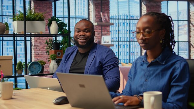 African american couple work on a management project together, using a laptop to research business trends and manage an online brand. Successful remote career development as a team. Camera A.