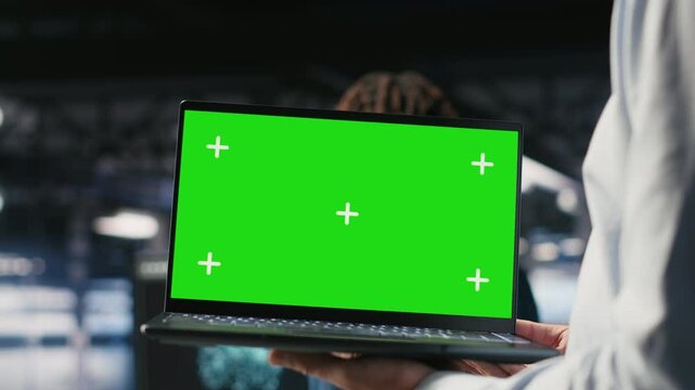 Close up of data center employee doing maintenance tasks on green screen laptop, ensuring optimal performance. Worker using mockup notebook to review diagnostics and apply patches, camera B
