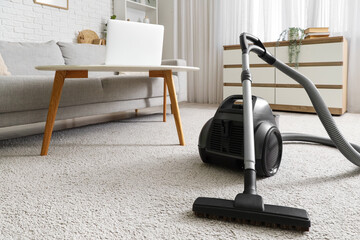 Interior of light living room with vacuum cleaner, sofa and commode