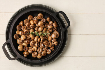 Frying pan with roasted mushrooms and rosemary on white wooden background