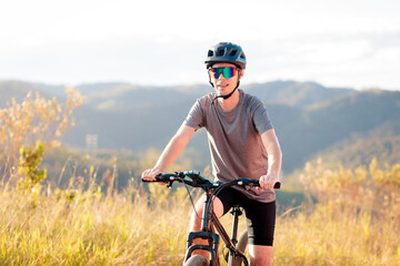 Man cycling on a dirt trail surrounded by nature, during golden hour. Concept of healthy lifestyle,...
