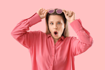 Wondering young woman with eyeglasses on pink background