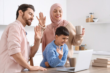 Happy Muslim family with laptop video chatting in kitchen
