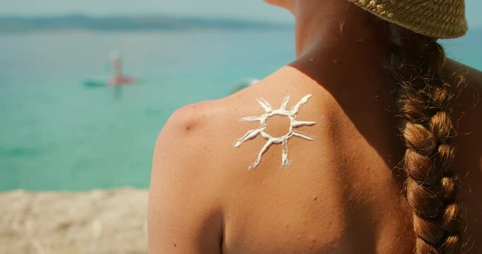 Back of woman with sunscreen sun design on shoulder by seaside in summer sunny day