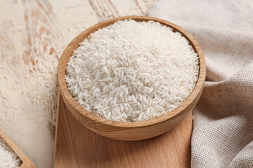 Bowl with raw rice on white wooden background