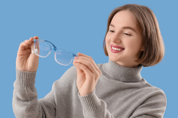 Beautiful young happy woman with new eyeglasses on blue background