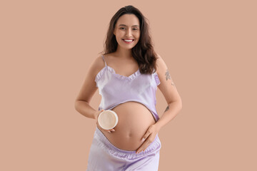 Young pregnant woman with body cream on beige background