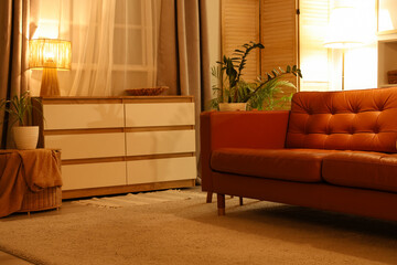Cozy sofa, chest of drawers and glowing lamps in interior of living room