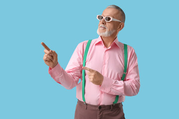 Senior man in sunglasses with suspenders pointing at something on blue background. National Grandpa...