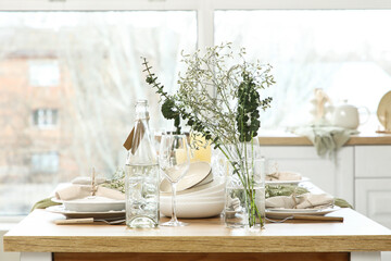Elegant table setting with beautiful flowers, eucalyptus branches and candles in light kitchen, closeup