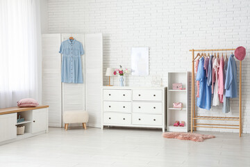 Interior of light dressing room with clothes rack, chest of drawers and folding screen