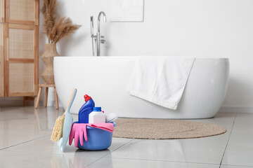 Plastic basin with cleaning supplies on floor in bathroom