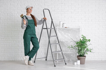 Female worker with paint brush and stepladder near white brick wall