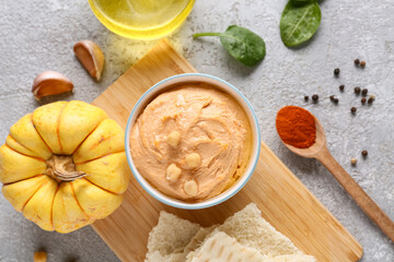 Bowl of tasty hummus with pumpkin, spinach and crackers on grey background
