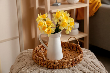 Wicker tray with vase of beautiful yellow daffodils bouquet on ottoman in room