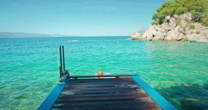 Woman in swimsuit jumping off dock into clear turquoise sea on sunny summer day