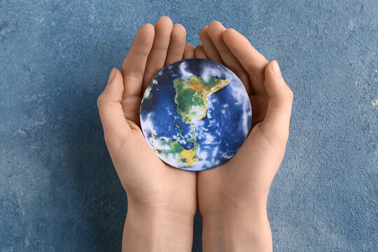 Female hands with paper model of Earth on grunge blue background. World Environment Day