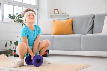 Sporty little boy trying to pick up heavy dumbbell at home